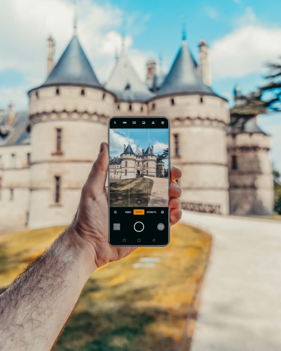 Mano che tiene uno smartphone OPPO in modalità fotocamera, inquadrando un castello della Loira. L’edificio storico è visibile sia sullo schermo del telefono sia sullo sfondo reale, con le sue torri coniche e l’architettura fiabesca. L’immagine, ambientata nella Valle della Loira, fa parte di una campagna di comunicazione per OPPO dedicata alla fotografia in viaggio.